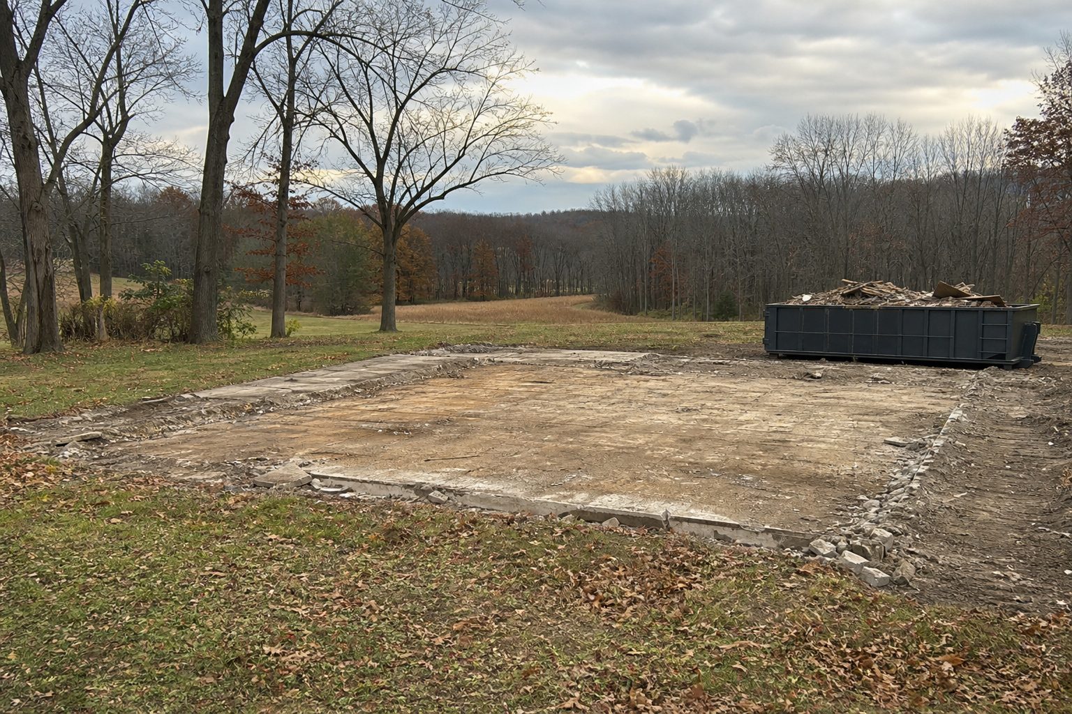 Cleared site after a structure was demolished, with debris container and bare footprint